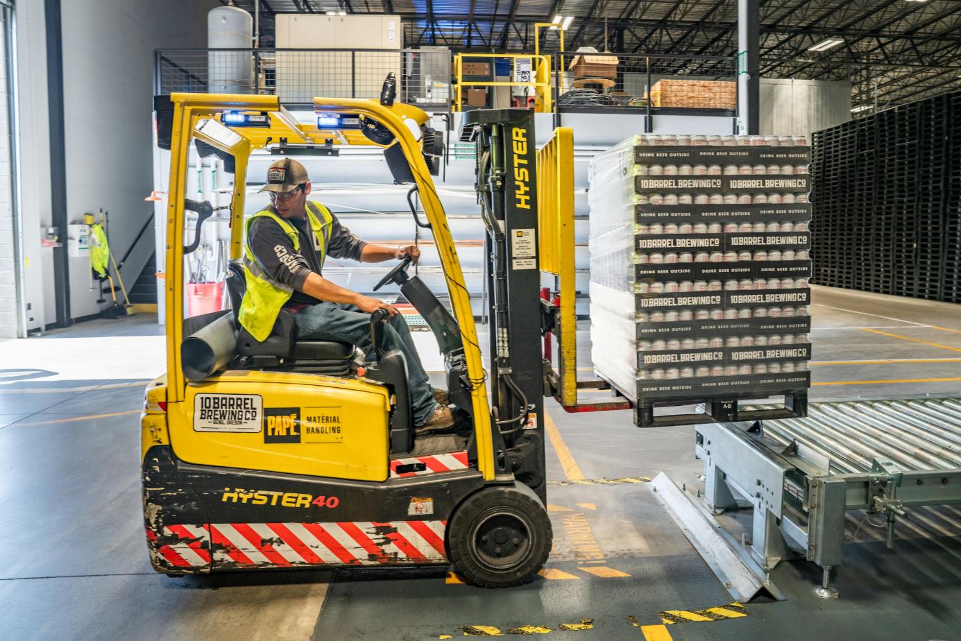 Magazijnmedewerker verplaatst stapel blikjes op kunststof pallet met heftruck in logistieke hal