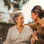 Oudere vrouw en mantelzorger lachen samen buiten in de tuin, symbool voor zorgunit nabijheid