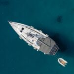 Zeiljacht van bovenaf gezien, drijvend op helderblauw water met klein bijbootje ernaast