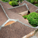 Bruin pannendak van traditioneel Aziatisch gebouw met decoratieve dakranden en omringend groen