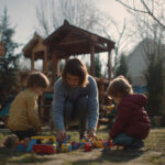 Jonge kinderen spelen buiten met speelgoed terwijl een ouder toezicht houdt in de tuin.
